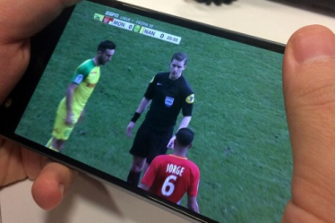 ایک آدمی ڈیجیٹل ایپلی کیشنز کے ذریعے اپنے سیل فون پر فٹ بال دیکھ رہا ہے۔