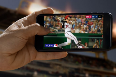 Човек који користи апликације да гледа бејзбол са свог мобилног телефона